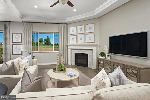 living room featuring a tray ceiling, crown molding, a high end fireplace, and dark wood-type flooring