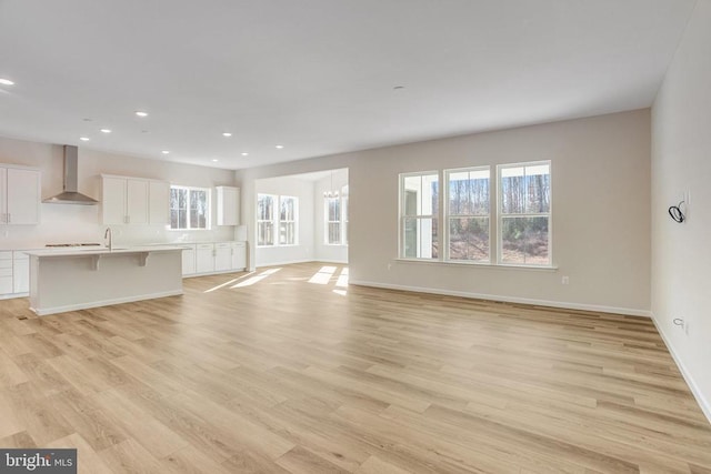 unfurnished living room with sink, a healthy amount of sunlight, a notable chandelier, and light hardwood / wood-style floors