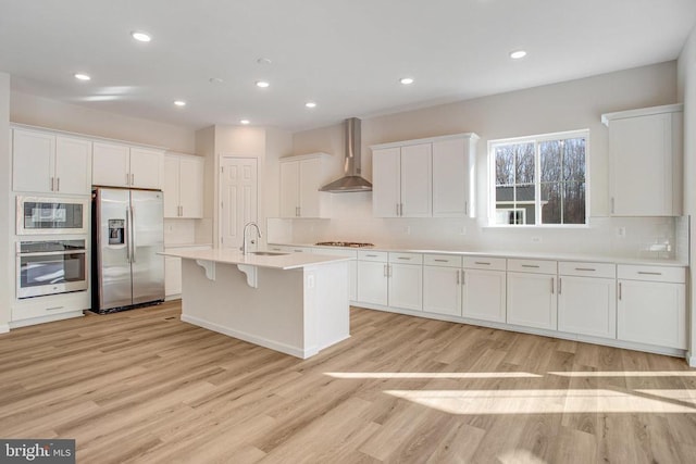 kitchen featuring white cabinets, wall chimney range hood, sink, light wood-type flooring, and stainless steel appliances