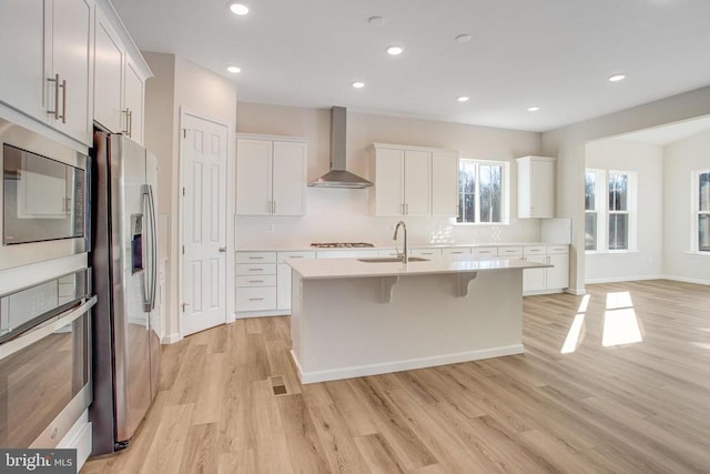 kitchen with white cabinetry, sink, wall chimney exhaust hood, a center island with sink, and appliances with stainless steel finishes