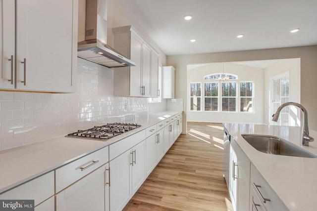 kitchen with appliances with stainless steel finishes, wall chimney exhaust hood, sink, white cabinets, and light hardwood / wood-style floors