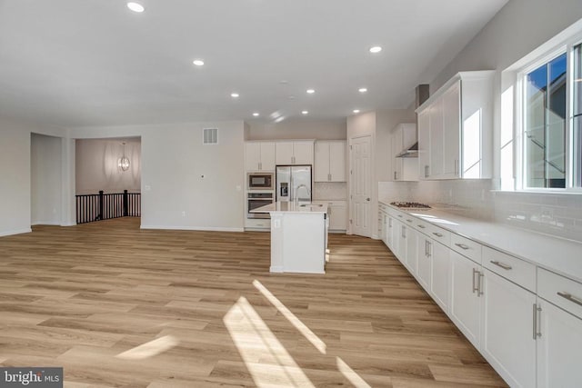 kitchen featuring a kitchen island with sink, white cabinets, light wood-type flooring, appliances with stainless steel finishes, and tasteful backsplash