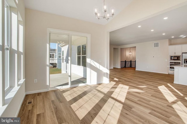 unfurnished living room with an inviting chandelier, lofted ceiling, and light wood-type flooring