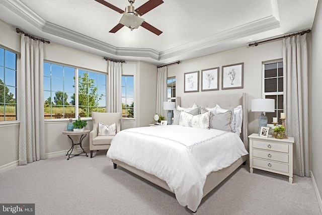 carpeted bedroom with a raised ceiling, multiple windows, ceiling fan, and ornamental molding