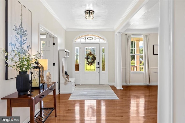 foyer entrance featuring wood-type flooring, crown molding, and ornate columns