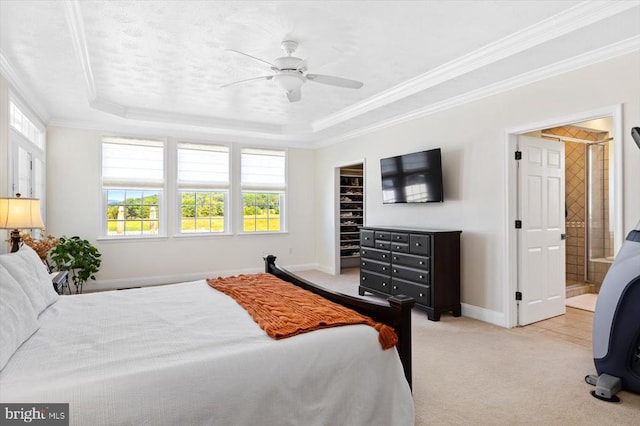 carpeted bedroom featuring a spacious closet, a tray ceiling, crown molding, connected bathroom, and ceiling fan