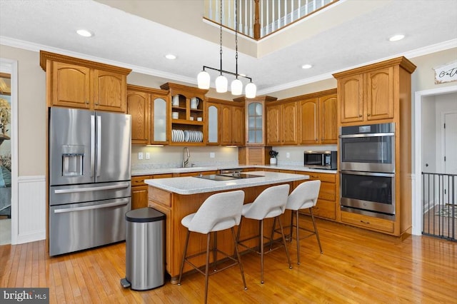 kitchen featuring pendant lighting, ornamental molding, stainless steel appliances, a center island, and light hardwood / wood-style floors