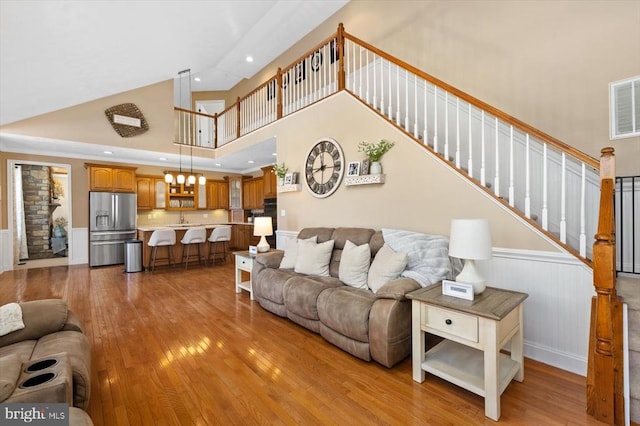 living room with a high ceiling, sink, a chandelier, and light hardwood / wood-style flooring