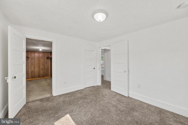 unfurnished bedroom with a spacious closet, wood walls, carpet floors, a textured ceiling, and a closet