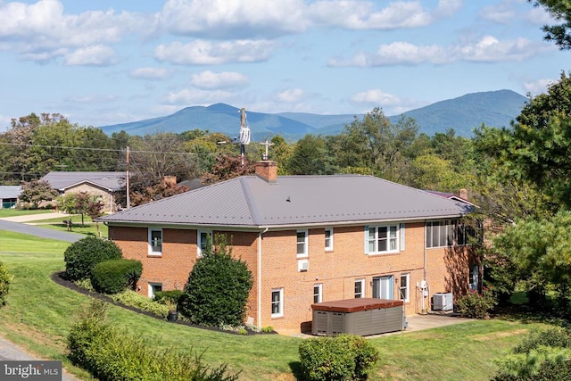 back of house with a mountain view, a lawn, and a hot tub