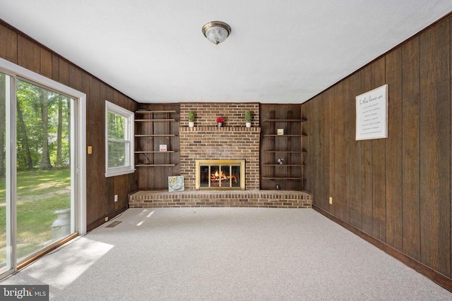 unfurnished living room featuring light carpet, a brick fireplace, built in shelves, and wooden walls