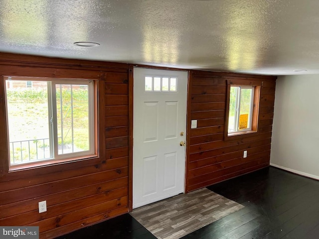 entrance foyer with a textured ceiling, dark wood-type flooring, a healthy amount of sunlight, and wooden walls