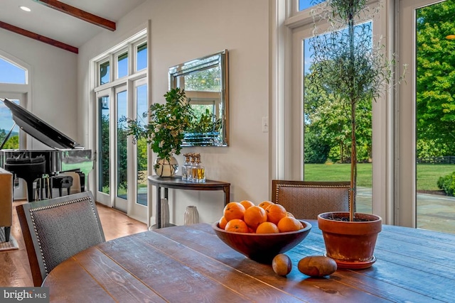 dining room with wood-type flooring, vaulted ceiling with beams, and a healthy amount of sunlight