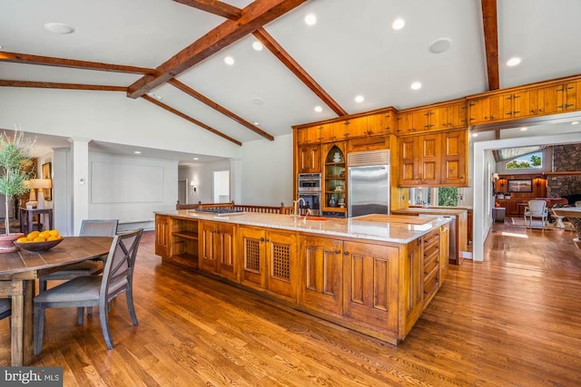 kitchen with lofted ceiling with beams, a large island, hardwood / wood-style flooring, stainless steel appliances, and light stone countertops