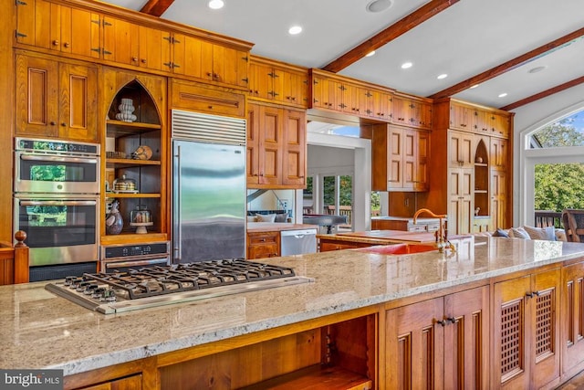 kitchen featuring light stone counters, beamed ceiling, appliances with stainless steel finishes, and sink