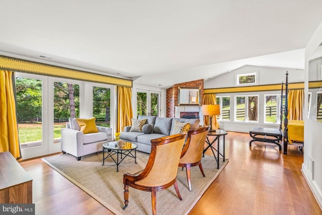 living room with lofted ceiling, light wood-type flooring, a fireplace, and a wealth of natural light