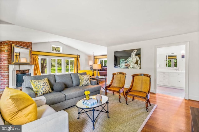 living room featuring a brick fireplace, vaulted ceiling, and hardwood / wood-style flooring