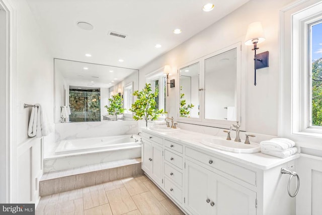 bathroom with a relaxing tiled tub, vanity, and a wealth of natural light