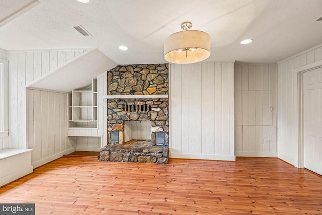 living room featuring lofted ceiling, wood walls, a textured ceiling, a fireplace, and light hardwood / wood-style floors