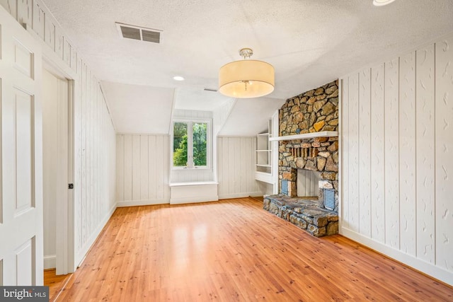 unfurnished living room featuring wood-type flooring, vaulted ceiling, a textured ceiling, and a fireplace