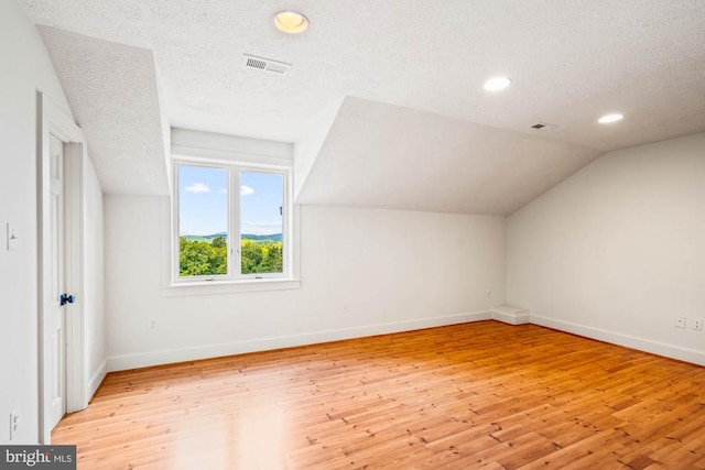 bonus room featuring light wood-type flooring, lofted ceiling, and a textured ceiling