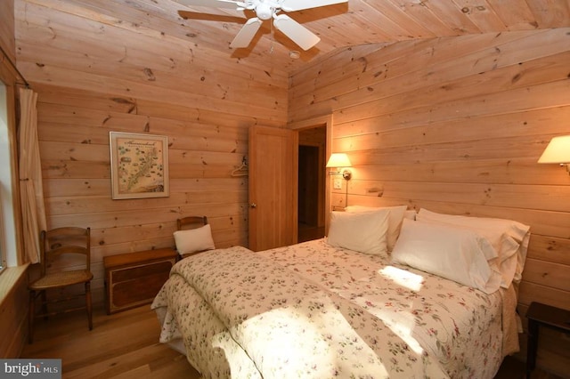 bedroom with light wood-type flooring, lofted ceiling, ceiling fan, and wood walls