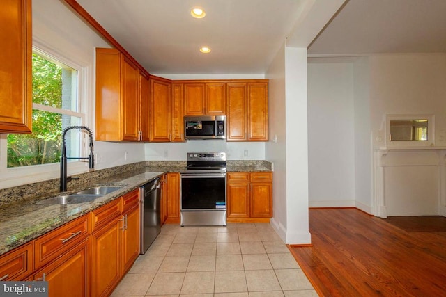 kitchen with appliances with stainless steel finishes, light wood-type flooring, stone countertops, and sink