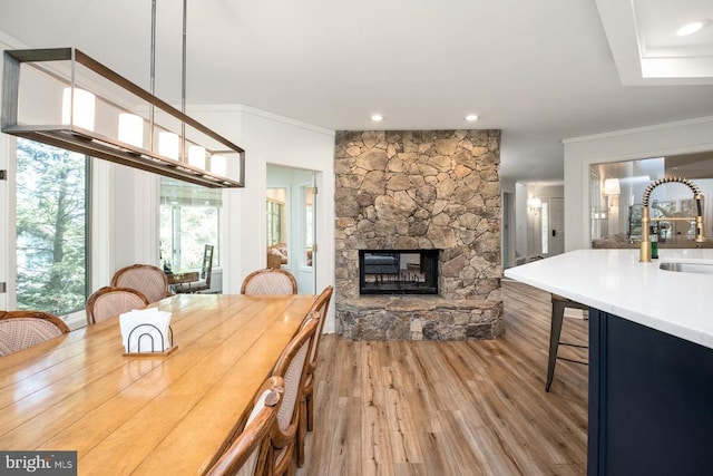 dining area featuring ornamental molding, sink, hardwood / wood-style floors, and a stone fireplace