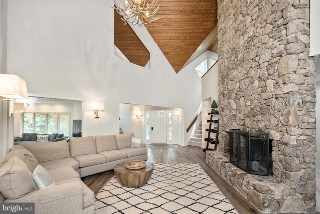 living room with wood ceiling, high vaulted ceiling, a stone fireplace, an inviting chandelier, and hardwood / wood-style flooring