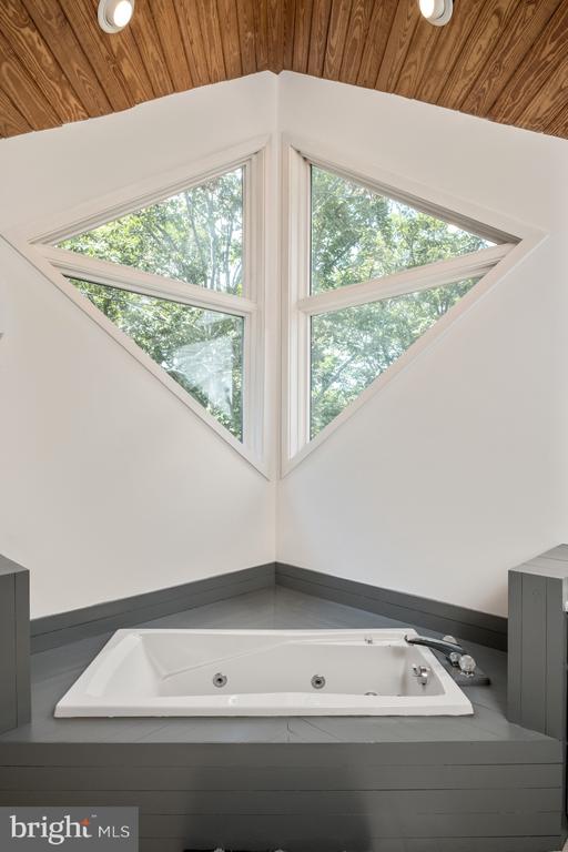 interior space with wood ceiling, vaulted ceiling, tiled bath, and a healthy amount of sunlight