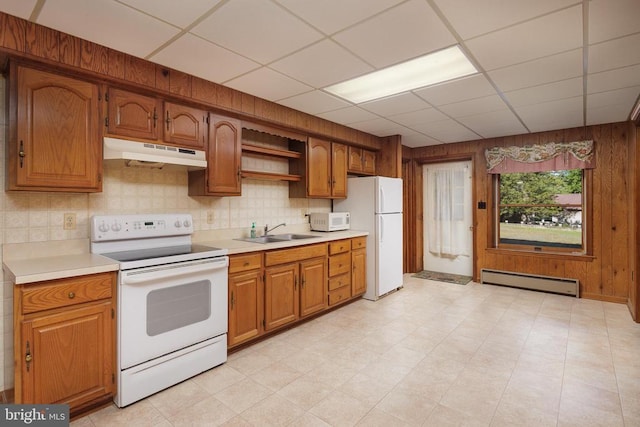 kitchen with a drop ceiling, white appliances, sink, wooden walls, and a baseboard radiator