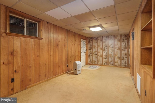 basement with a drop ceiling, carpet, and wooden walls