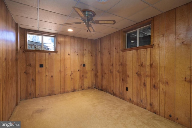 basement featuring wood walls, a paneled ceiling, carpet flooring, and ceiling fan