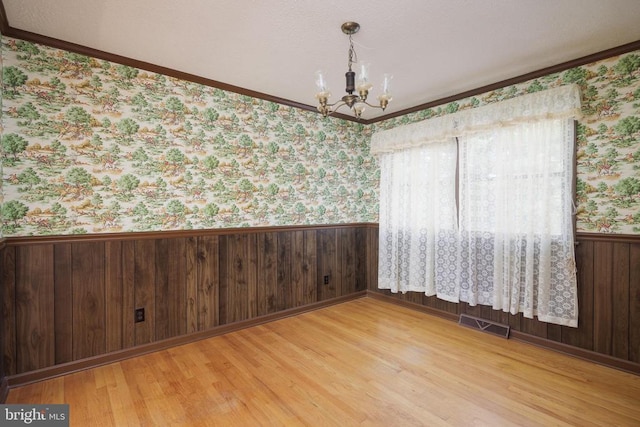 spare room featuring wood walls, ornamental molding, a chandelier, and light hardwood / wood-style floors