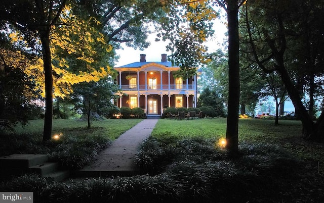 italianate home featuring a porch, a balcony, and a front yard