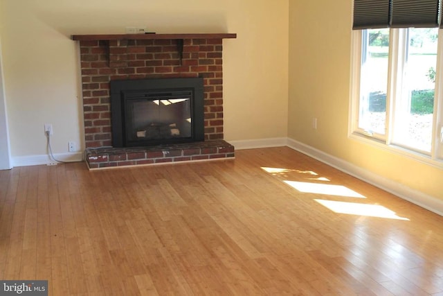 unfurnished living room with light wood-type flooring and a brick fireplace