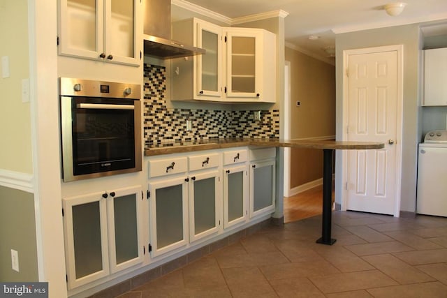 kitchen with white cabinetry, backsplash, stainless steel oven, crown molding, and washer / dryer