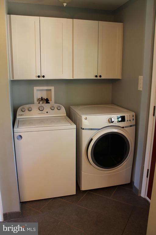 clothes washing area with cabinets, dark tile patterned flooring, and washing machine and clothes dryer