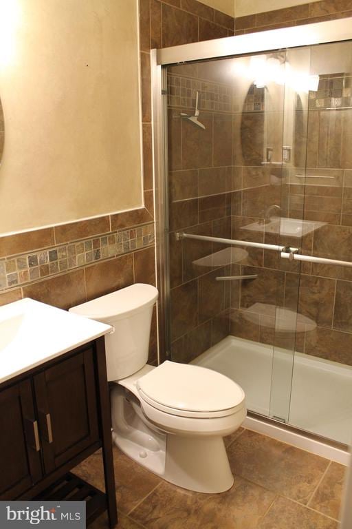 bathroom with tile walls, vanity, toilet, and a shower with door