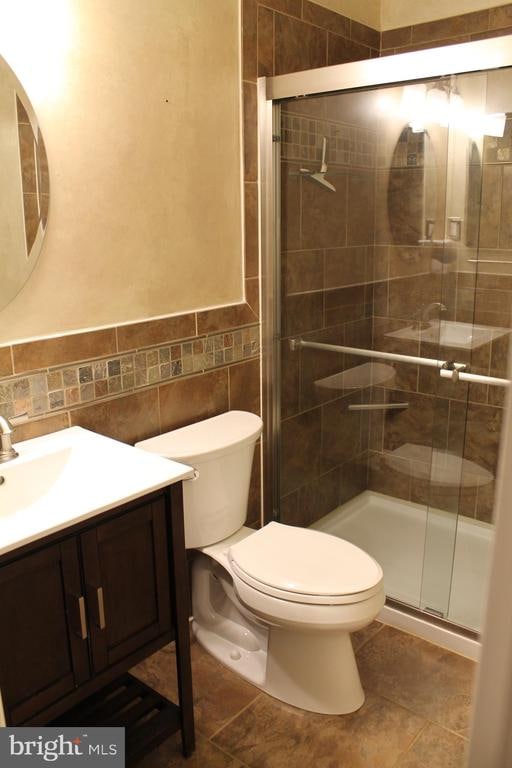 bathroom featuring vanity, toilet, tile walls, tile patterned flooring, and a shower with door