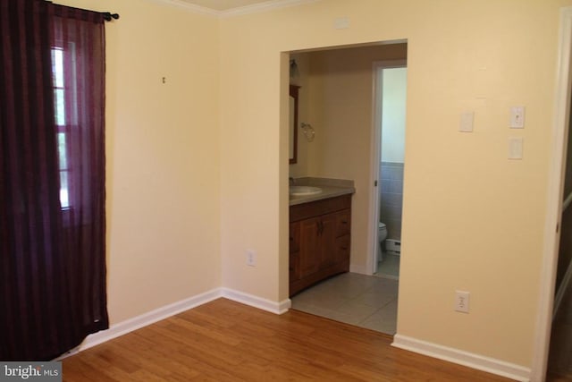 interior space featuring baseboard heating, ornamental molding, sink, and hardwood / wood-style flooring