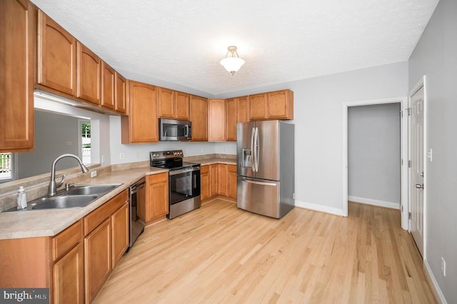 kitchen featuring appliances with stainless steel finishes, sink, light wood-type flooring, and a textured ceiling