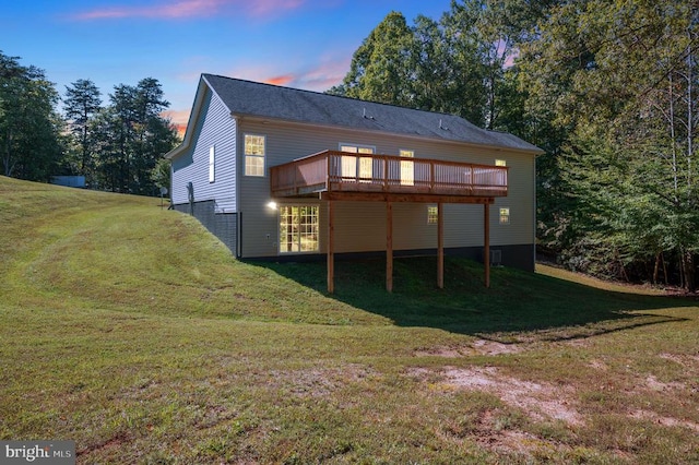 back house at dusk featuring a wooden deck and a yard