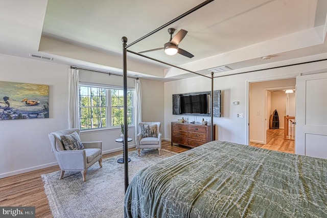 bedroom with ceiling fan, a raised ceiling, and light hardwood / wood-style floors