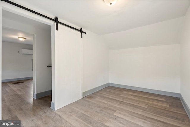 bonus room featuring an AC wall unit, light wood-type flooring, and a barn door