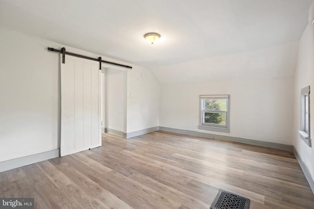 unfurnished bedroom with lofted ceiling, a barn door, and light wood-type flooring