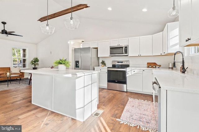 kitchen featuring a kitchen island, hanging light fixtures, white cabinets, light wood-type flooring, and appliances with stainless steel finishes