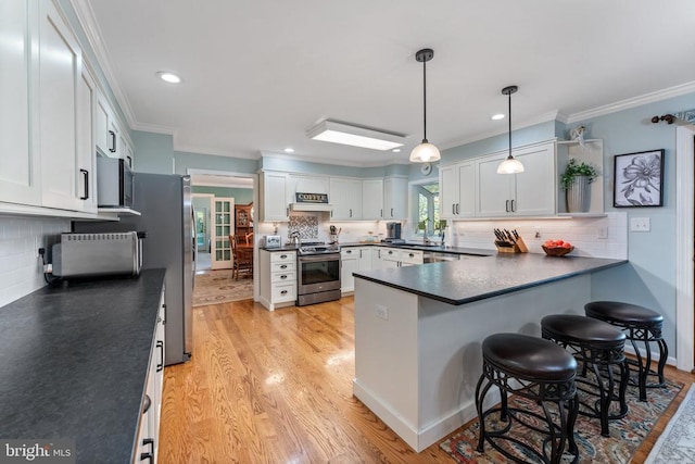 kitchen featuring a breakfast bar area, appliances with stainless steel finishes, white cabinetry, light wood-type flooring, and decorative light fixtures