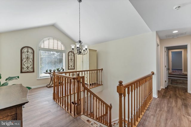 corridor with an inviting chandelier, lofted ceiling, and light hardwood / wood-style floors