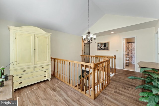 corridor with light hardwood / wood-style flooring, lofted ceiling, and an inviting chandelier